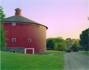 Round red barn with green grass in early evening or early morning with a dirt road next to it